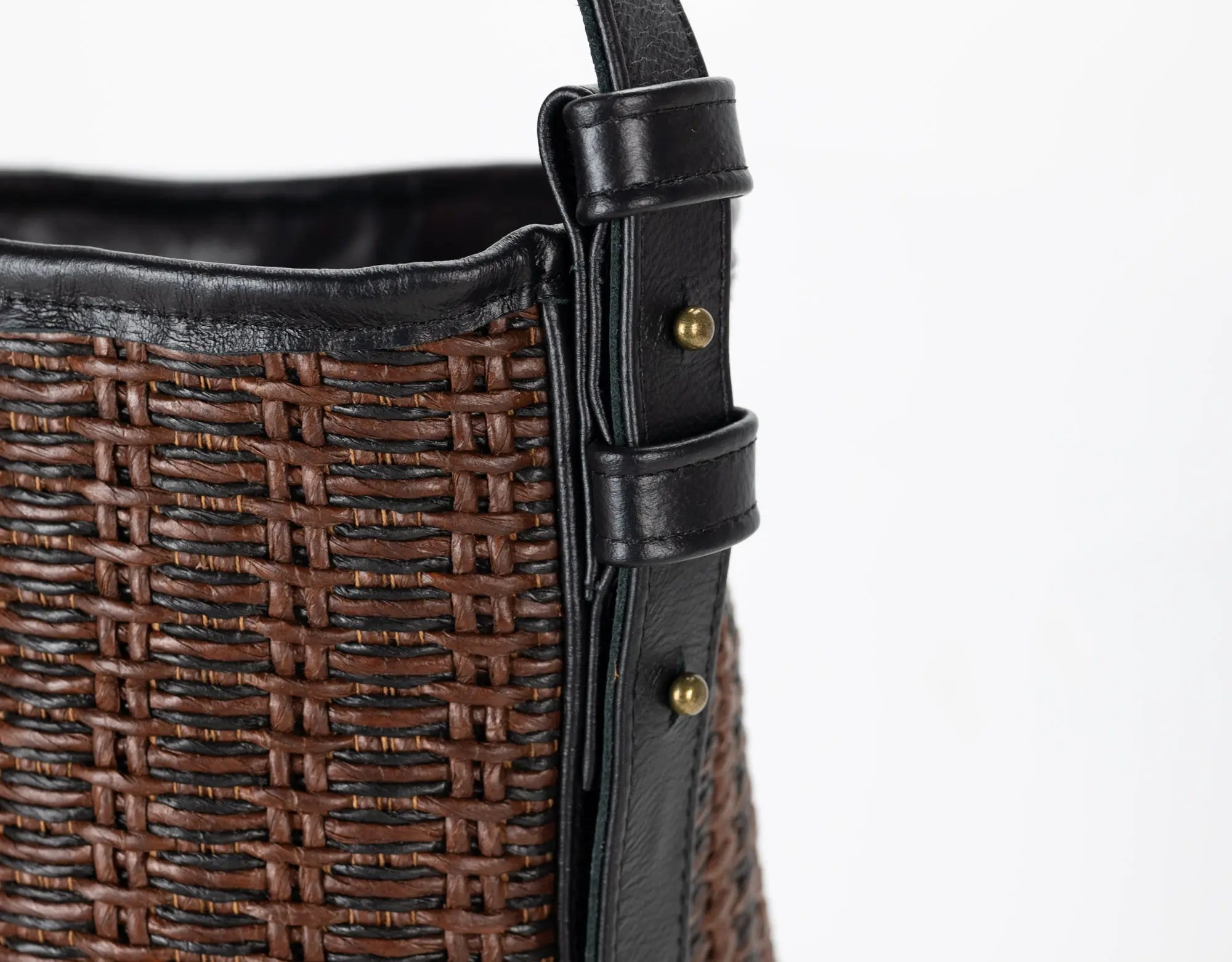 Brown woven handbag with black leather trim on a white background