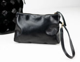 Black leather clutch bag with wrist strap on a white background