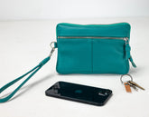 Teal leather crossbody bag with a phone and keys on a white background