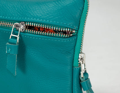 Close-up of a teal leather bag with a zipper on a light gray background