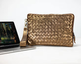 Gold woven clutch bag next to a laptop on a white background