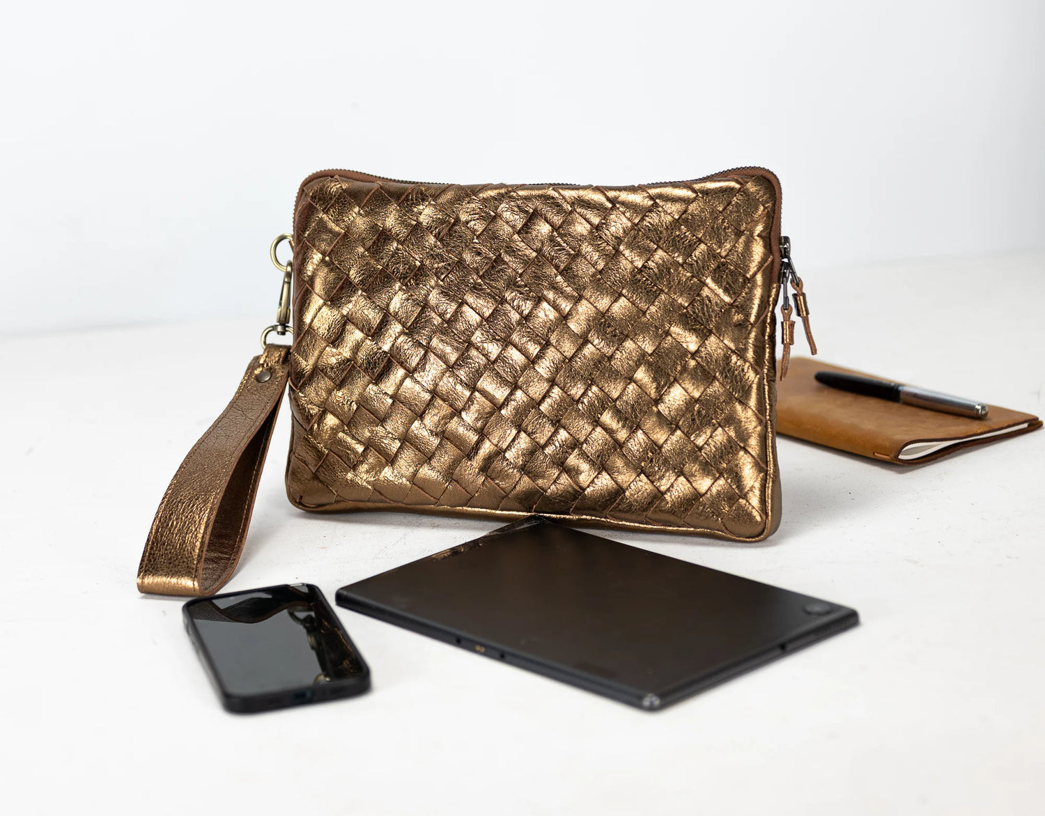 Gold woven clutch bag with phone, tablet, and notebook on a white background