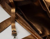 Close-up of a metallic bronze textured leather bag showing the interior zip pocket and strap attachment.