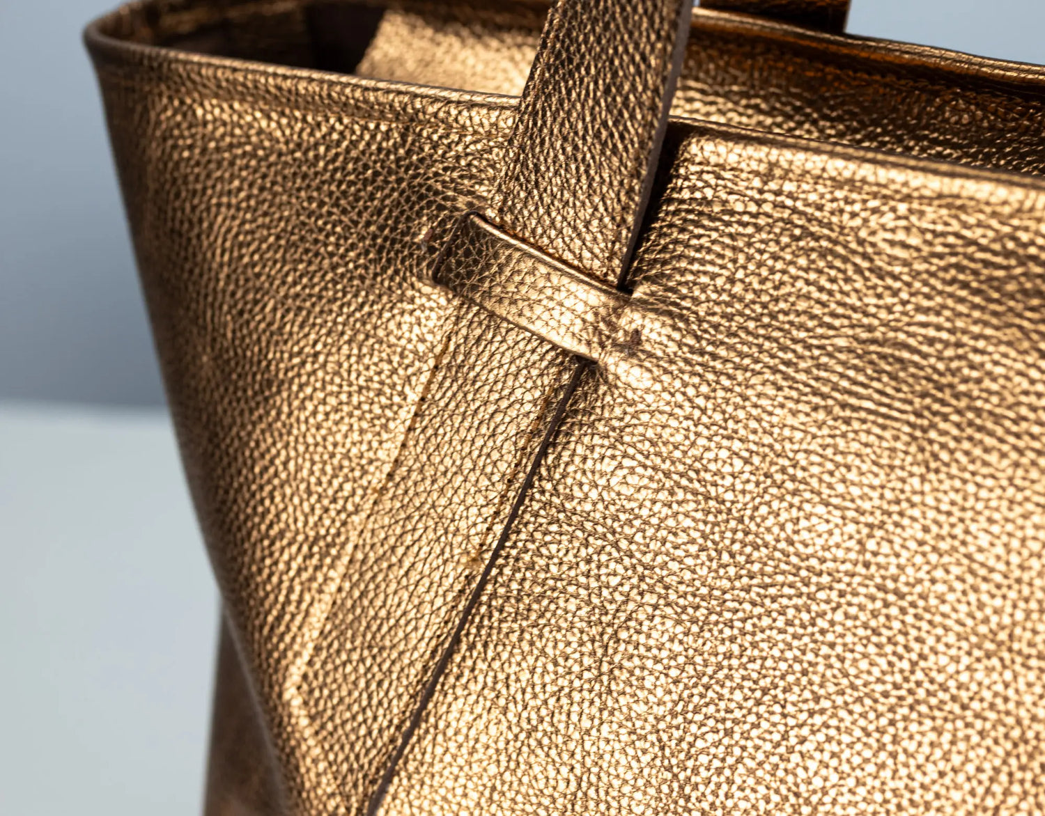 Close-up of a metallic gold pebbled leather tote bag showing the texture and strap attachment.