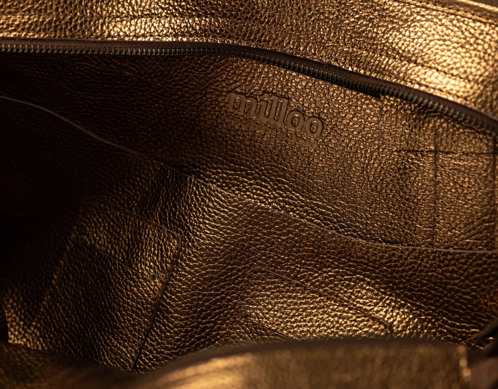 Close-up of the interior lining of a metallic bronze pebbled leather bag, showing the debossed brand name &
