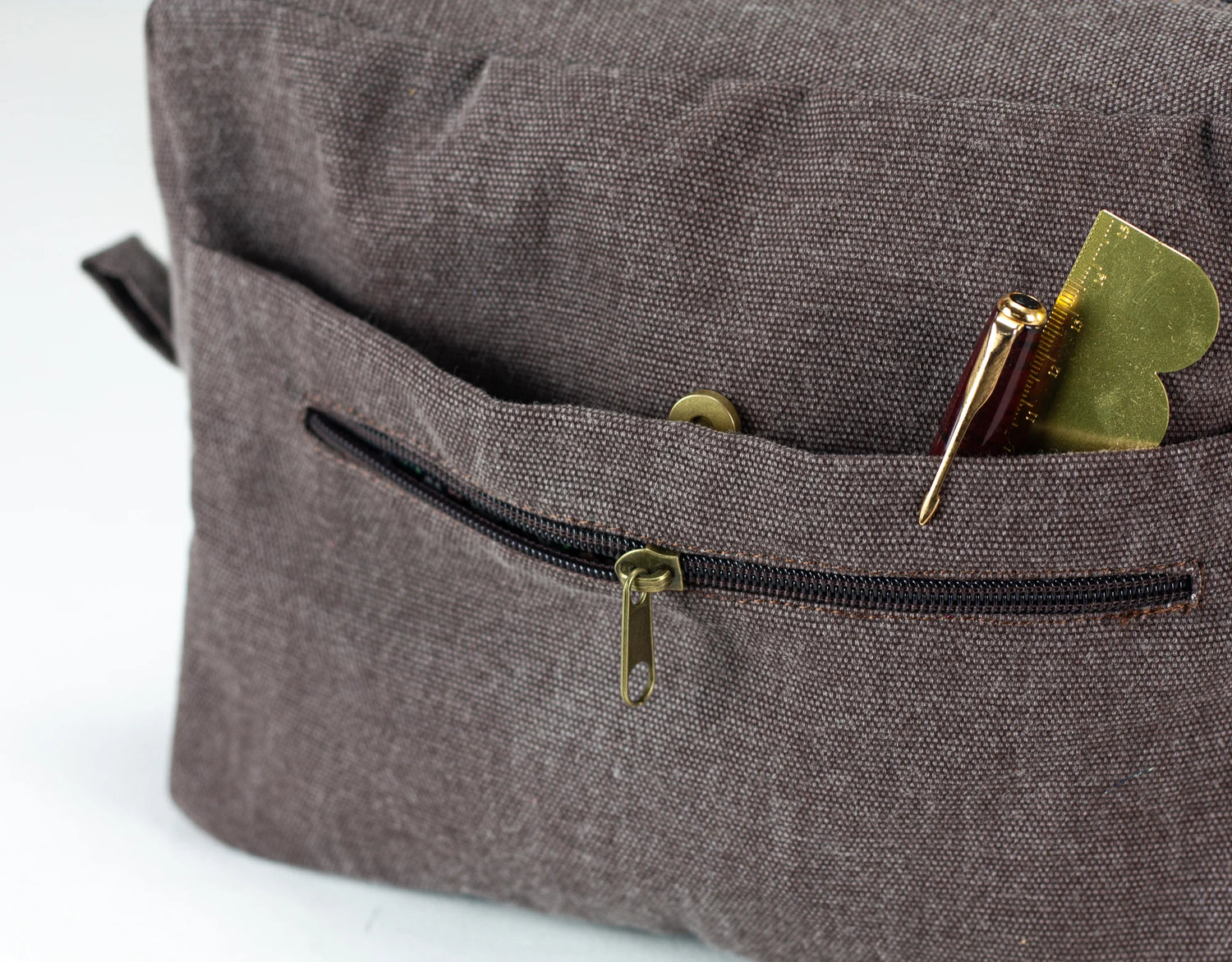 Close-up of a brown textured bag with a zipper pocket containing a pen  