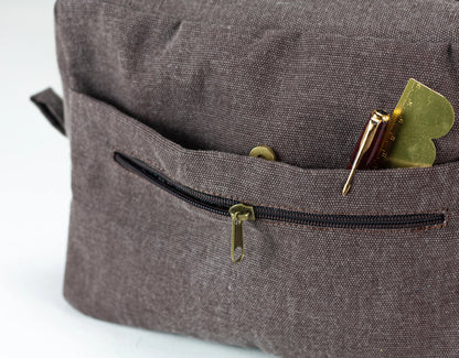 Close-up of a brown textured bag with a zipper pocket containing a pen  