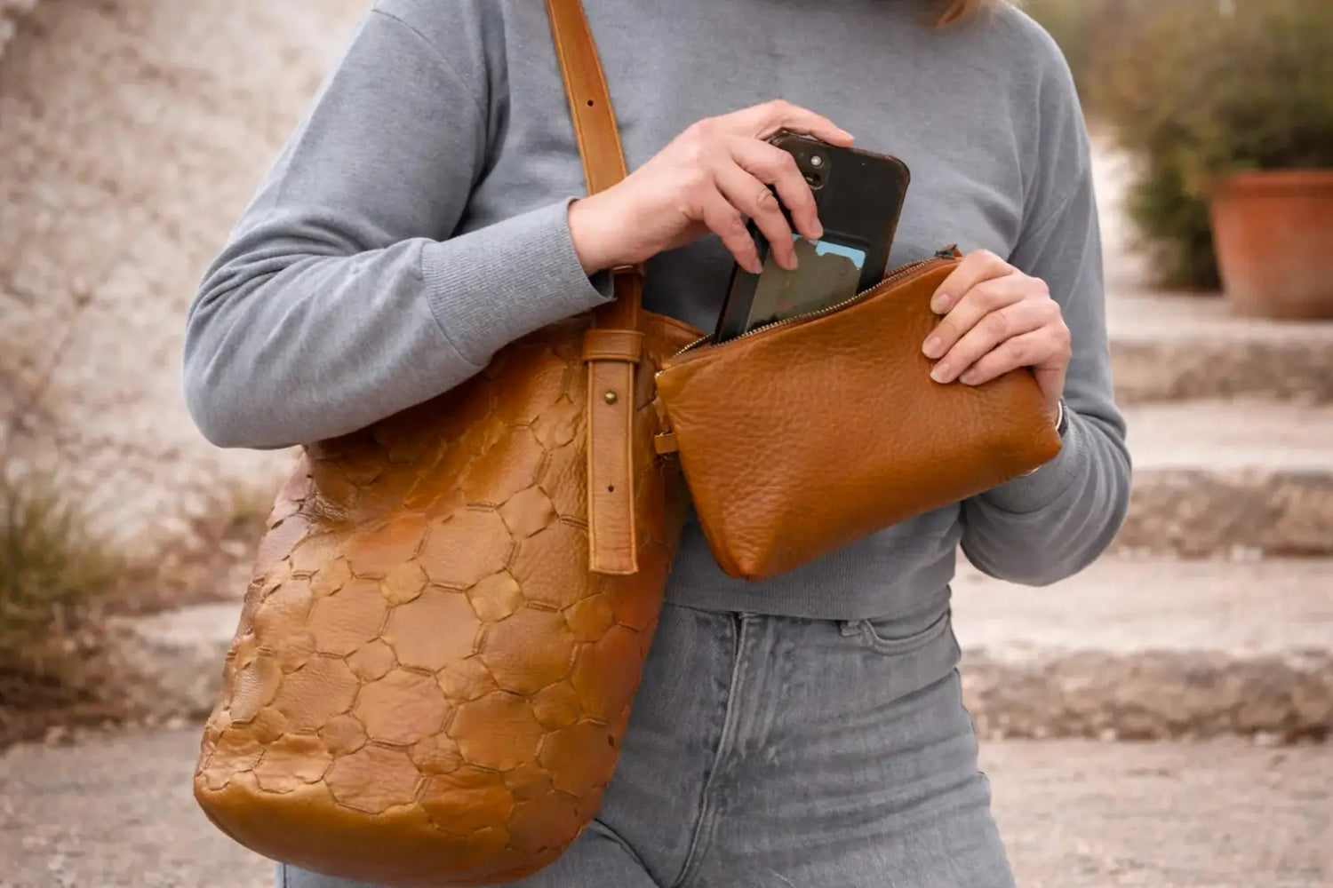 Person holding a brown leather bag with a phone case inside, outdoors.