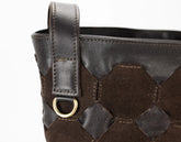 Brown leather handbag with geometric pattern and gold ring detail on a white background