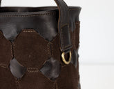 Close-up of a brown leather bag with decorative stitching and a gold ring on a white background