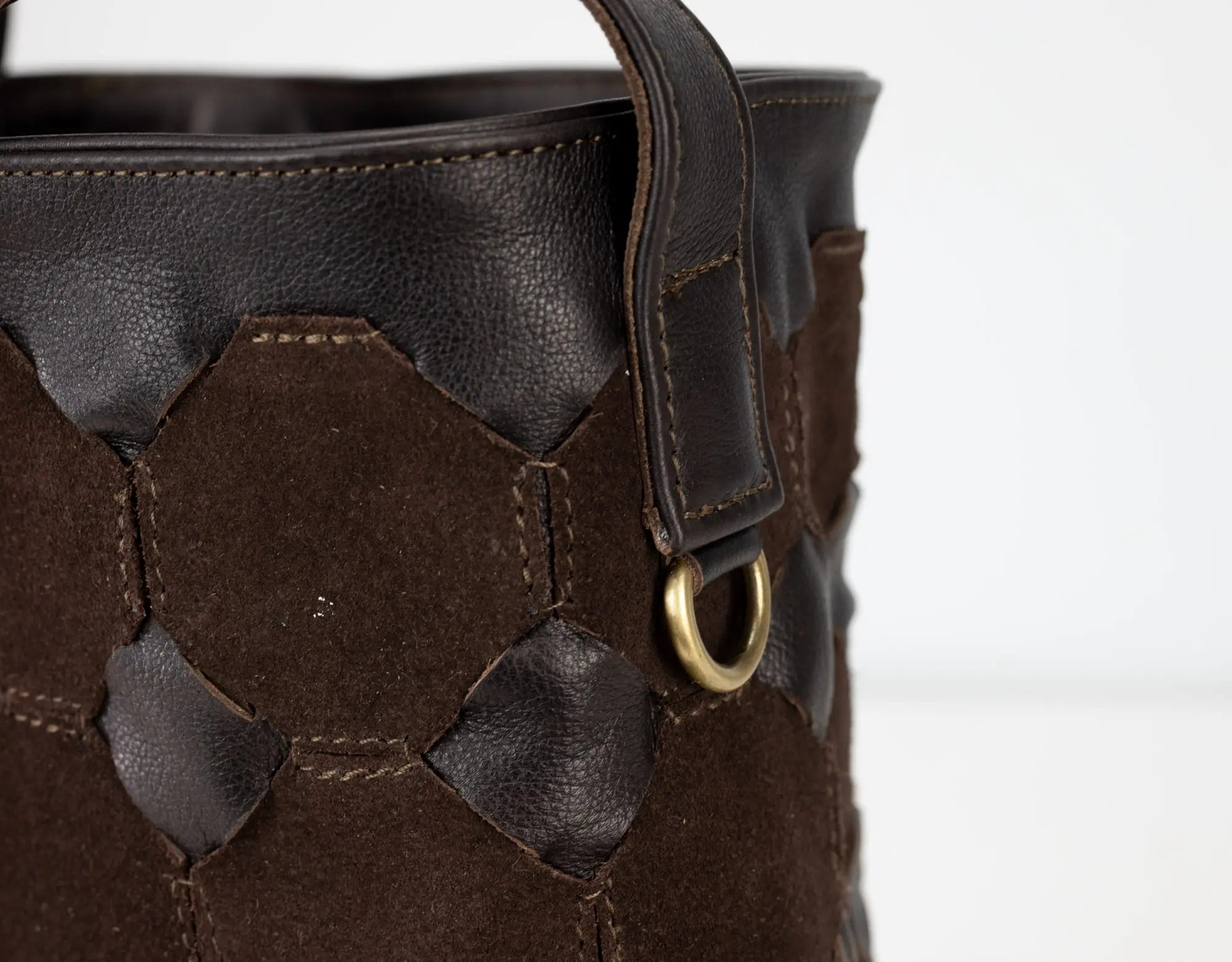 Close-up of a brown leather bag with decorative stitching and a gold ring on a white background