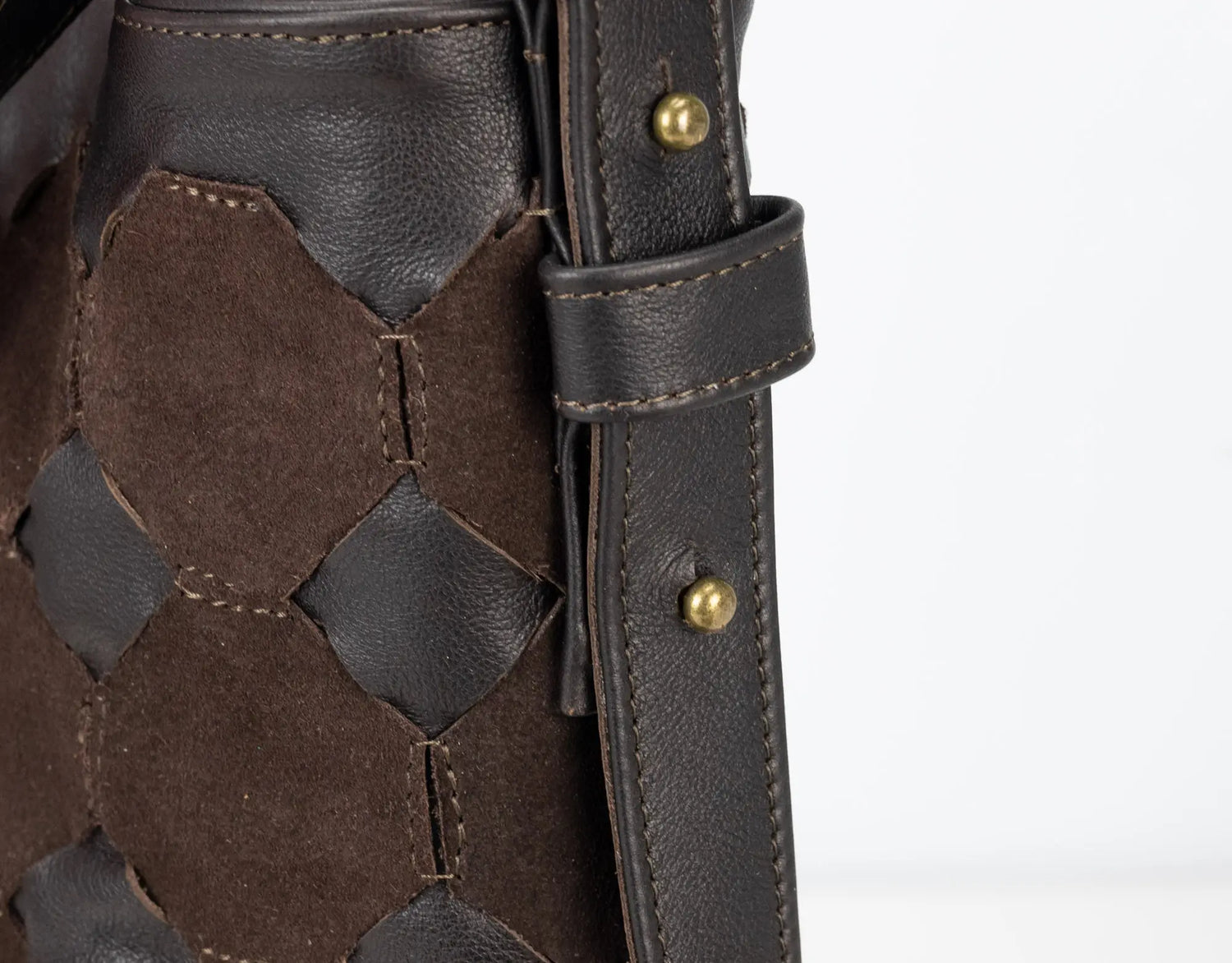 Close-up of a brown leather outfit with geometric pattern and gold buttons on a white background