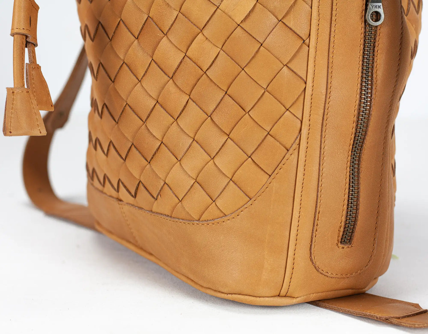 Close-up of a tan leather handbag with woven pattern and zipper on a white background