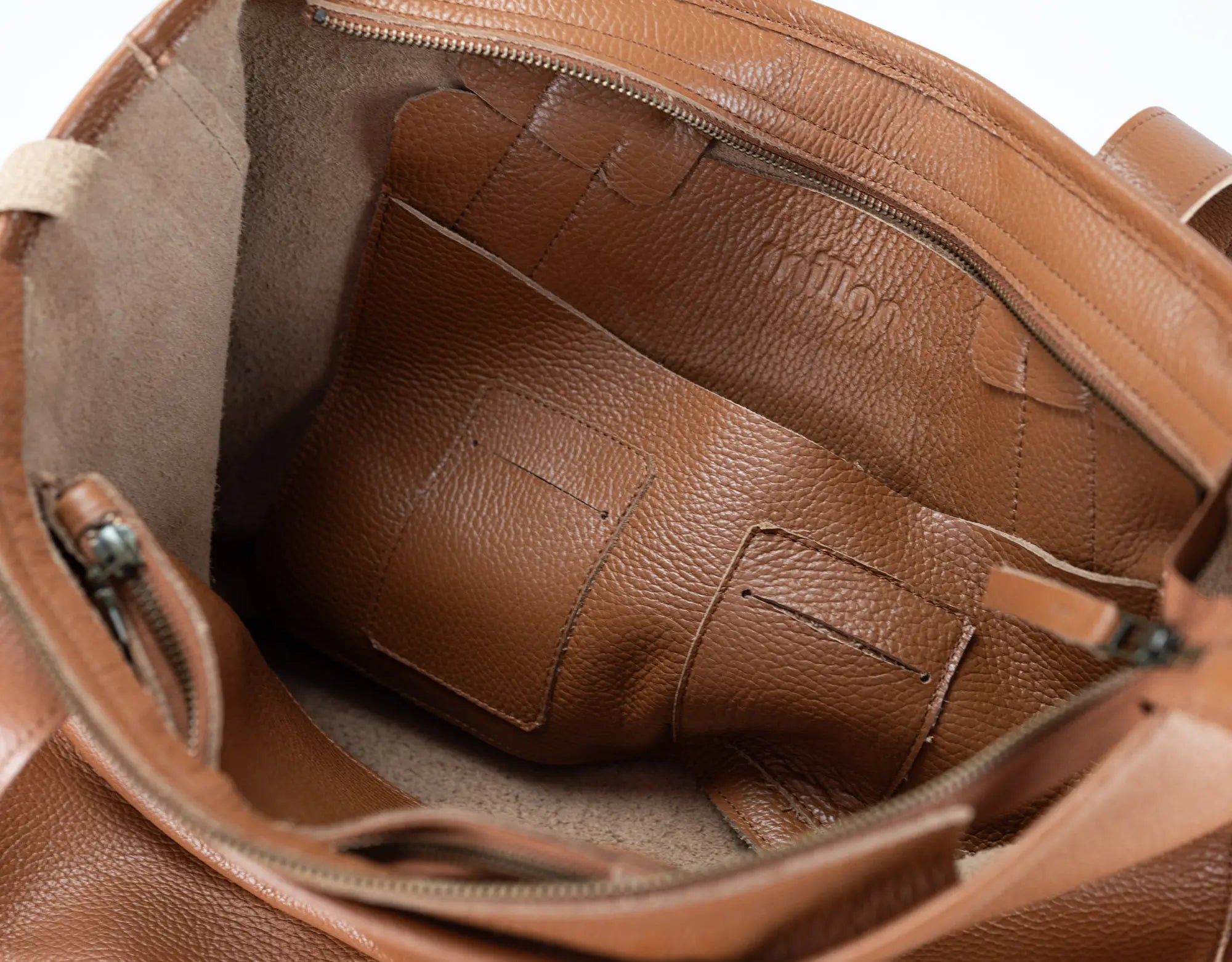 Close-up of the interior of a brown pebbled leather bag, showing the lining, zipper, and interior card slots.
