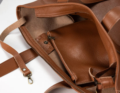 Close-up of a brown pebbled leather tote bag showing the interior compartments, zipper pockets, and strap attachments on a white background.