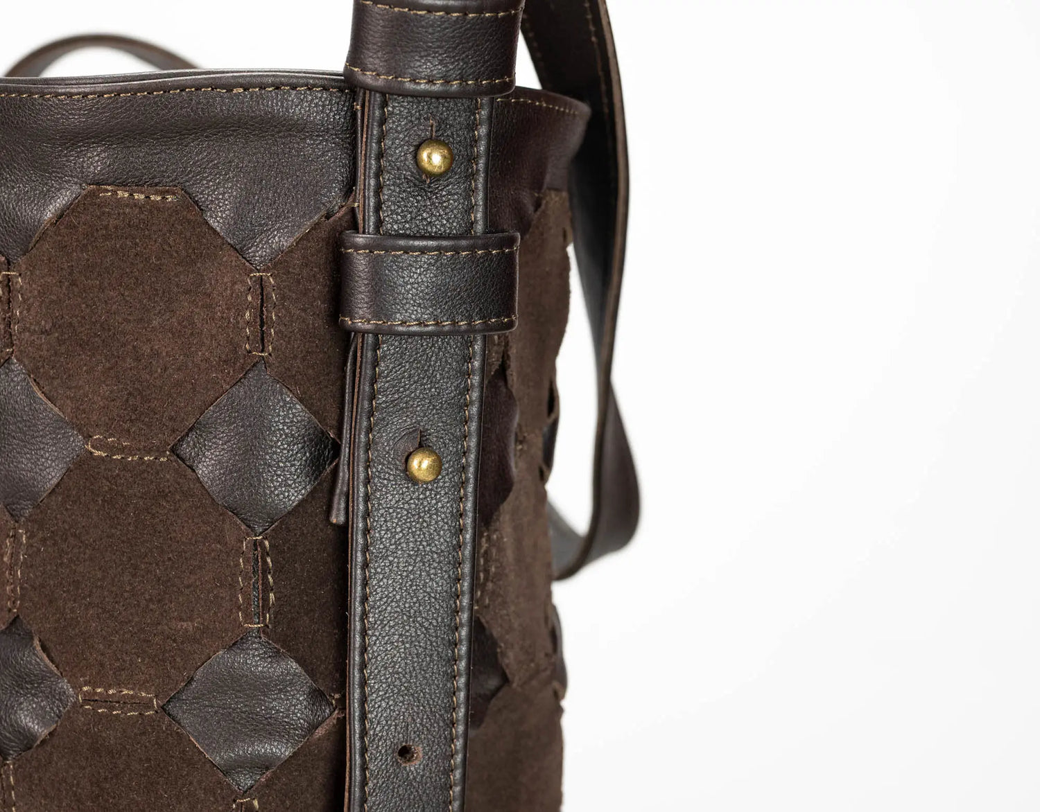 Close-up of a dark brown woven leather and suede bucket bag showing the strap attachment with brass rivets on a white background.