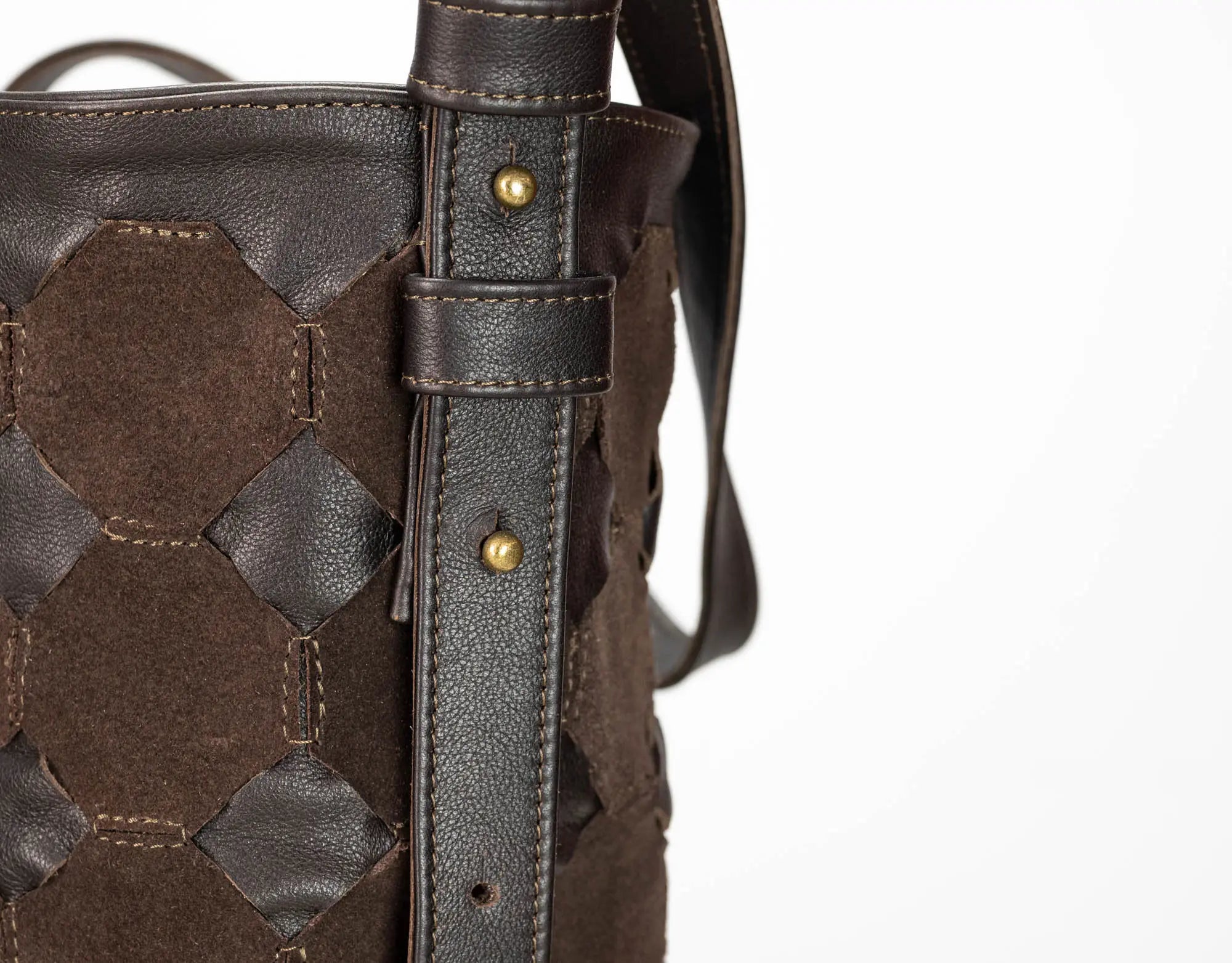 Close-up of a dark brown woven leather and suede bucket bag showing the strap attachment with brass rivets on a white background.