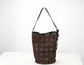 A dark brown leather bucket bag with a distinctive honeycomb pattern of stitched circular patches on the front, a black leather trim, and a single shoulder strap, set against a plain white background.