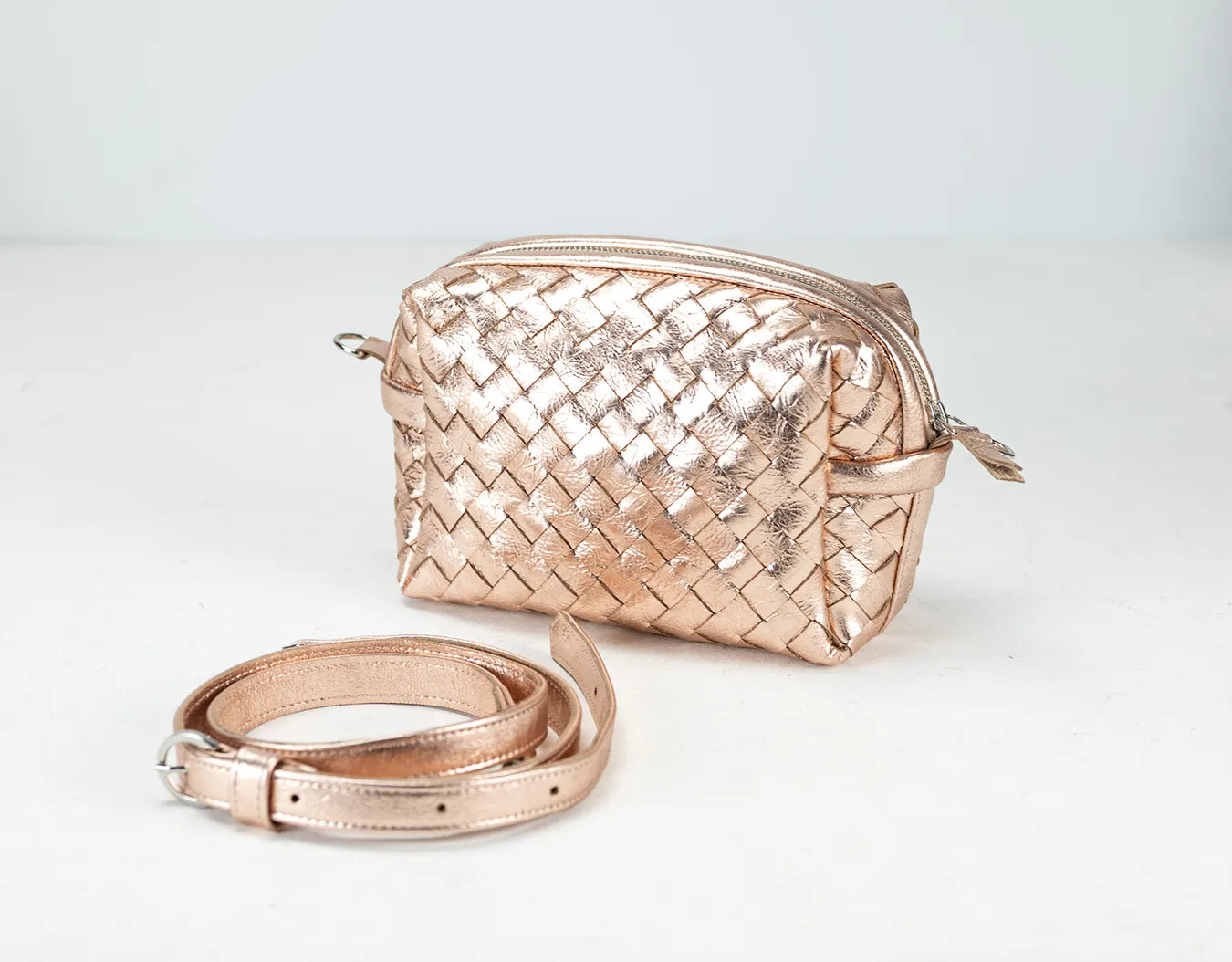 Rose gold woven handbag and matching belt on a light gray background