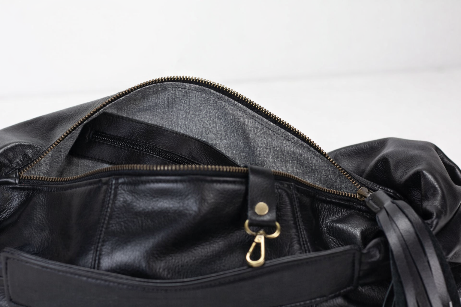 Close-up of a black leather bag with a gold zipper pull on a white background
