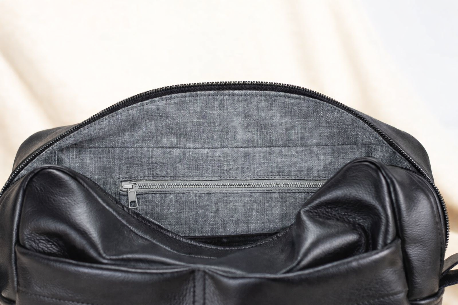 Black leather bag with zipper on a light beige background