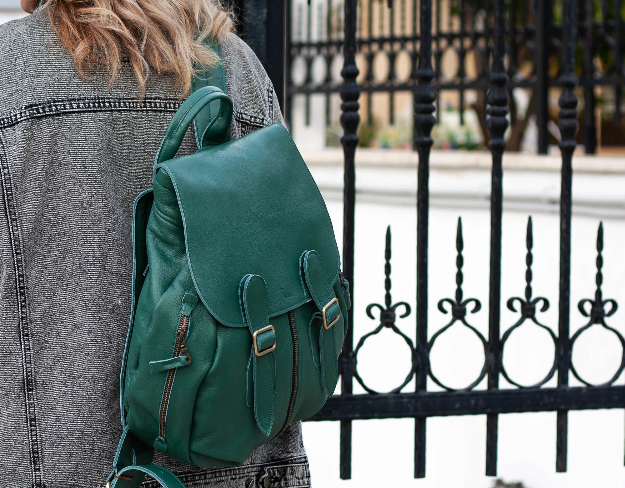 Green backpack worn by a person with a black metal fence in the background