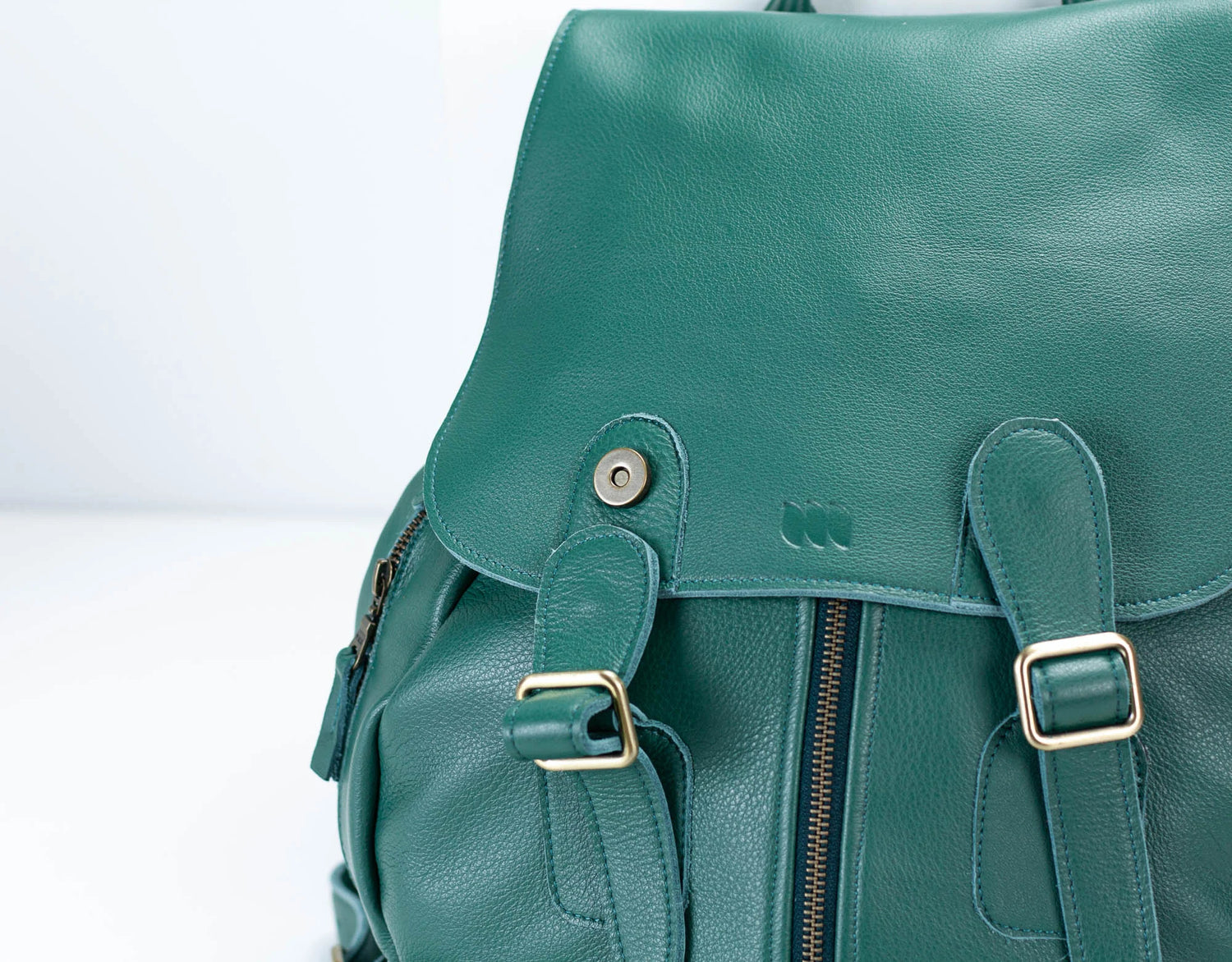 Green leather backpack with gold buckles on a light gray background