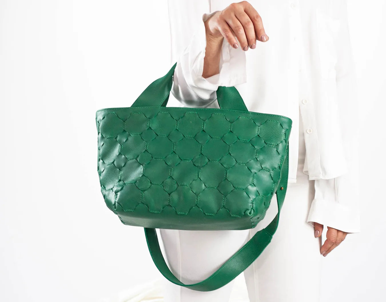 Green quilted handbag held by a person wearing a white outfit on a white background