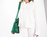 Person wearing a white outfit with a green handbag on a plain background