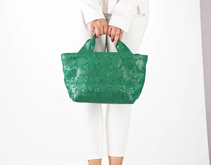 Green textured handbag held by a person wearing a white outfit on a light gray background