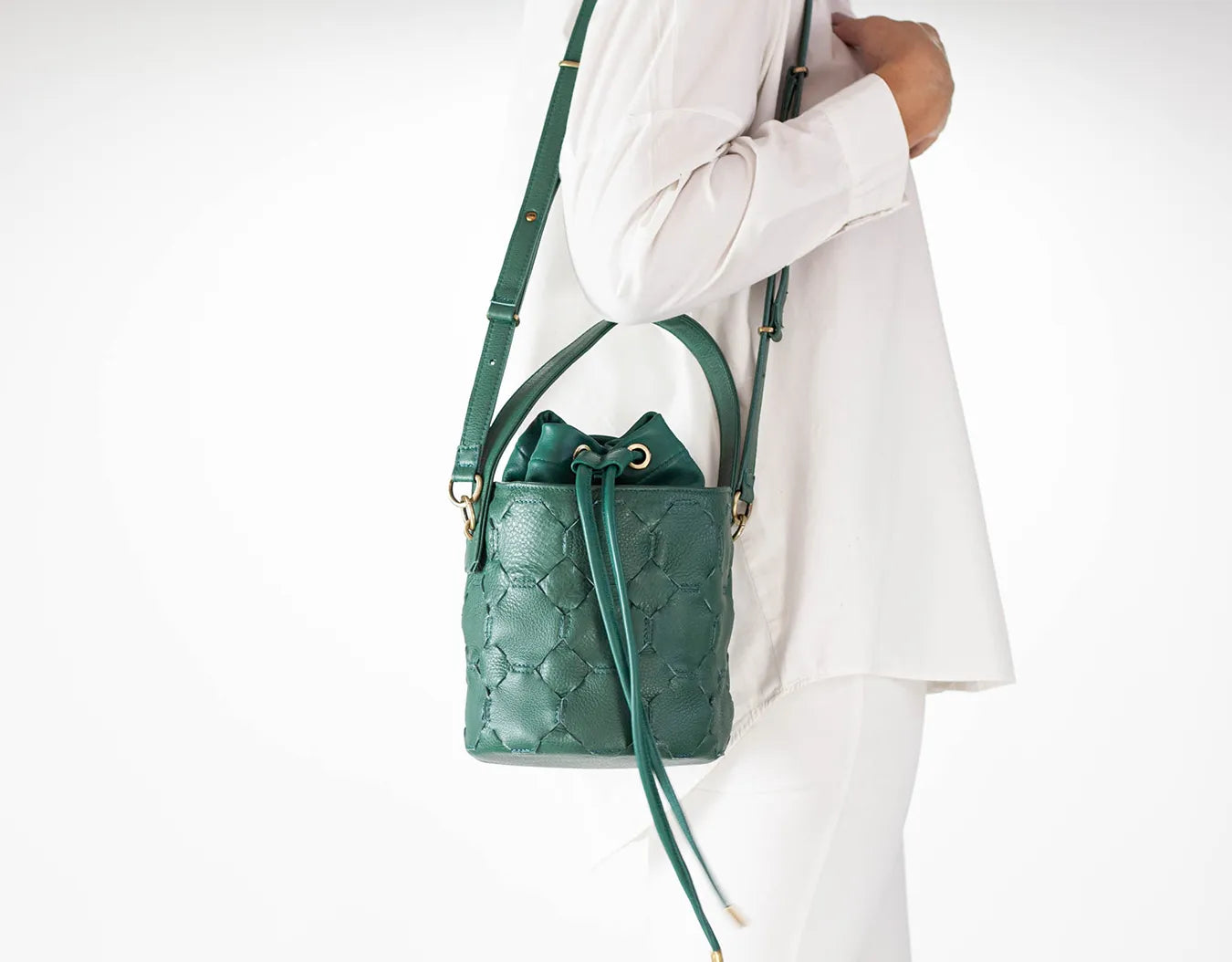 Green quilted handbag held by a person wearing a white outfit on a white background