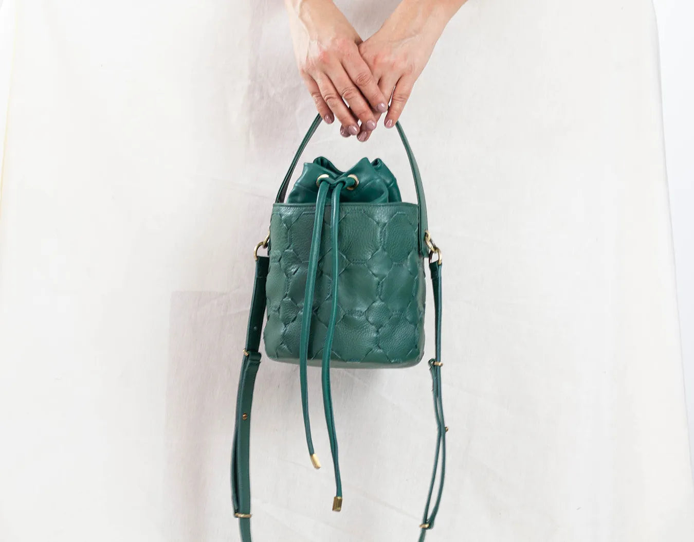 Green leather handbag held by a person against a white background