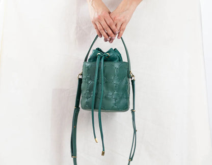 Green leather handbag held by a person against a white background