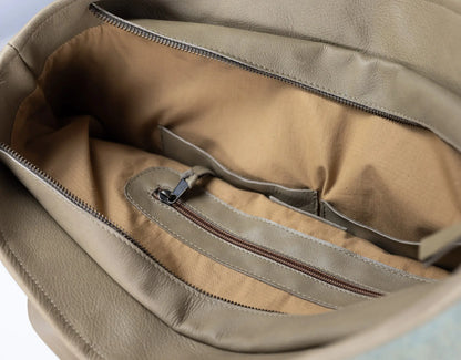 Close-up of the interior of a beige leather or faux-leather bag, showing a tan fabric lining, zippered compartments, and stitched pockets.