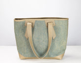 A tote bag with a textured sage green canvas body and light beige leather handles and trim, shown against a plain white background.