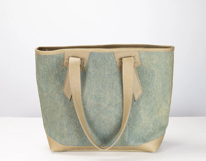 A tote bag with a textured sage green canvas body and light beige leather handles and trim, shown against a plain white background.