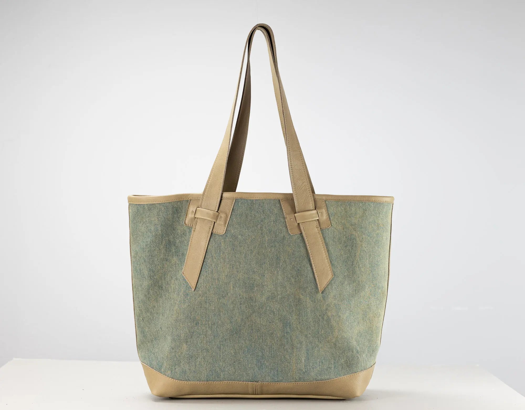 A canvas tote bag with a textured sage green body and tan leather handles and base, shown against a plain white studio background.