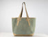 A canvas tote bag with a textured sage green body and tan leather handles and base, shown against a plain white studio background.