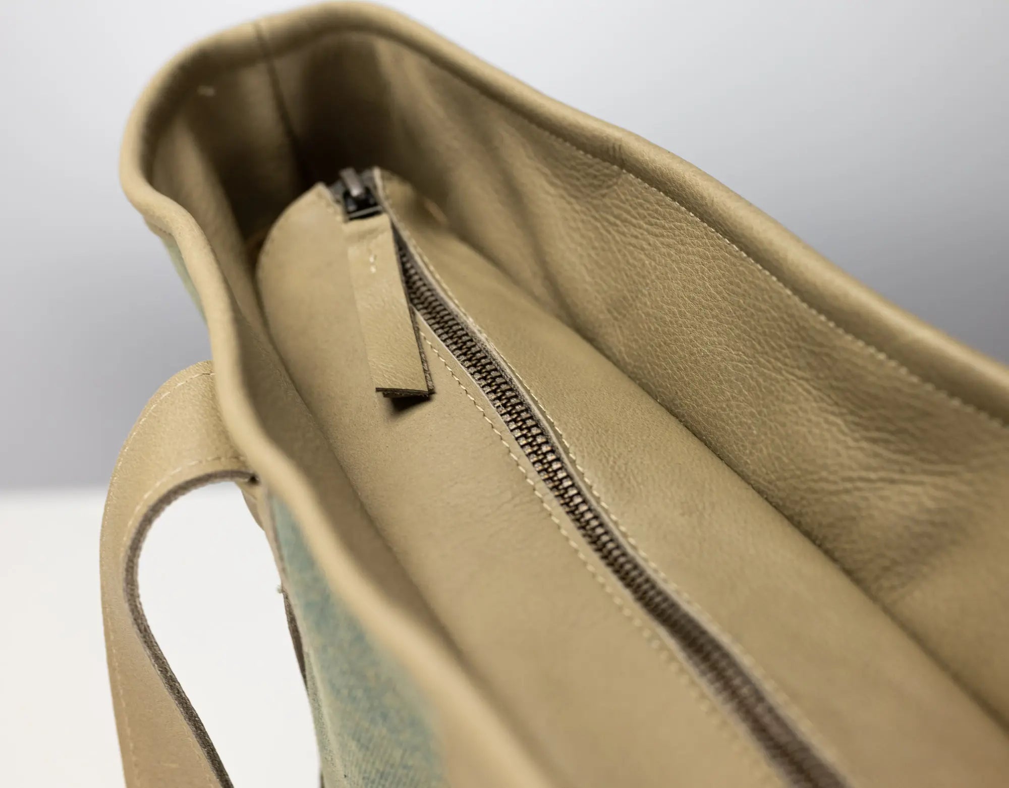 Close-up of the interior of a beige leather tote bag, showing a zippered compartment with a matching leather pull tab.