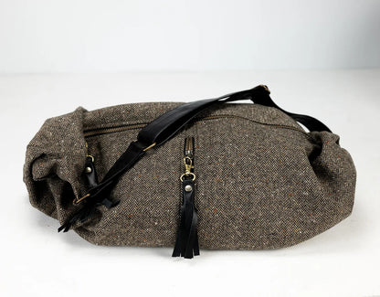 Brown waist bag with black straps and tassels on a white background