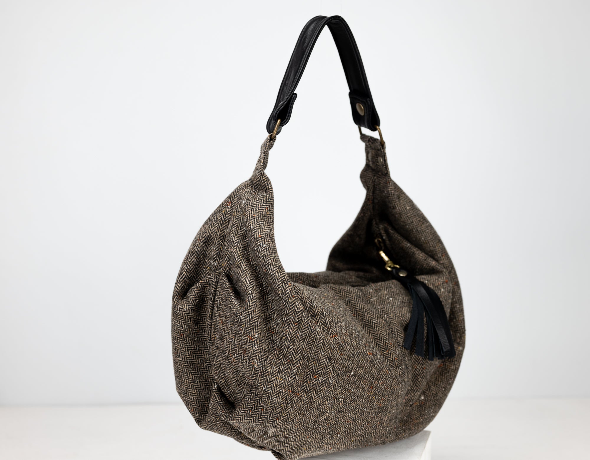 Brown textured handbag with black handle and tassel on a white background
