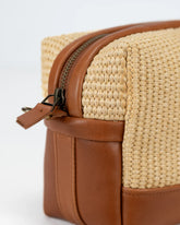 Close-up of a woven bag with brown leather accents on a white background
