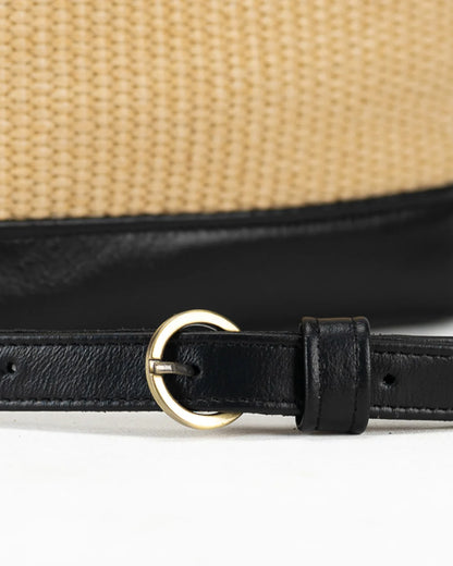 Close-up of a straw hat with a black leather strap and gold buckle on a white background