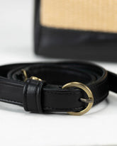 Black leather belt with a gold buckle on a white surface, with a straw hat in the background.