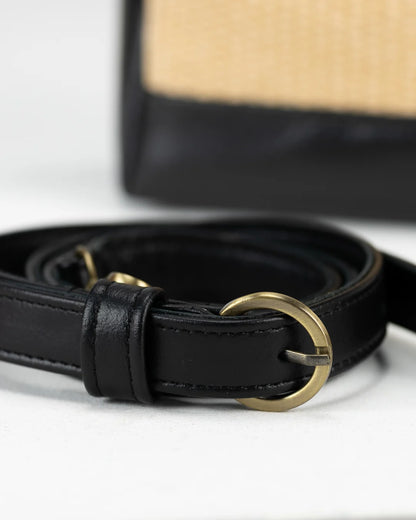 Black leather belt with a gold buckle on a white surface, with a straw hat in the background.
