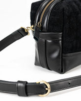 Black leather bag with gold zipper and belt on a white background