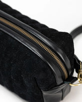 Black textured bag with gold zipper on a light gray background
