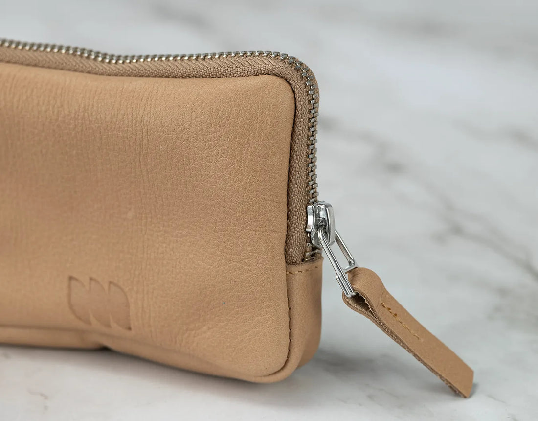 Close-up of a tan leather wallet with a zipper on a light marble background