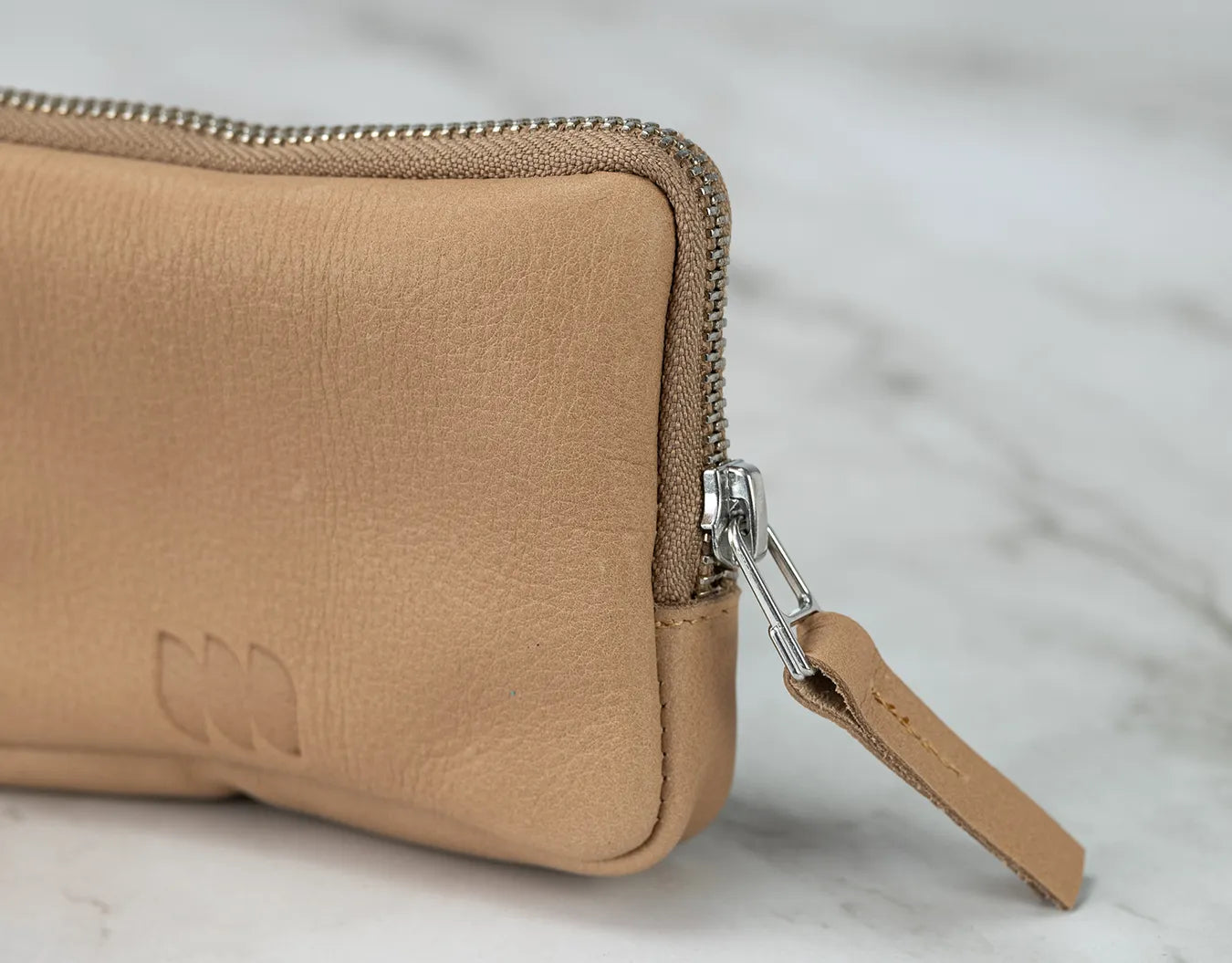 Close-up of a tan leather wallet with a zipper on a light marble background