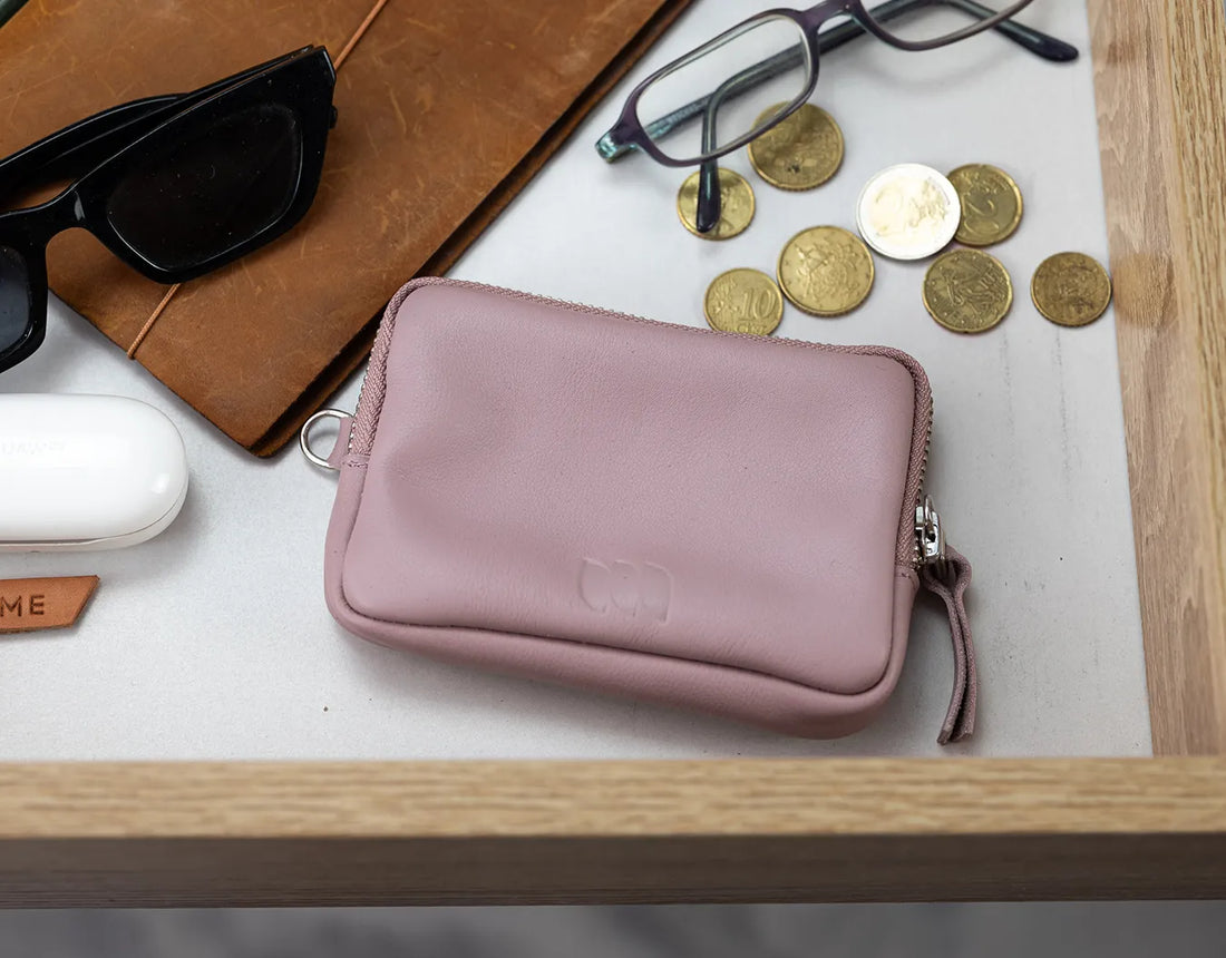 Pink wallet with sunglasses, notebook, and coins on a wooden surface